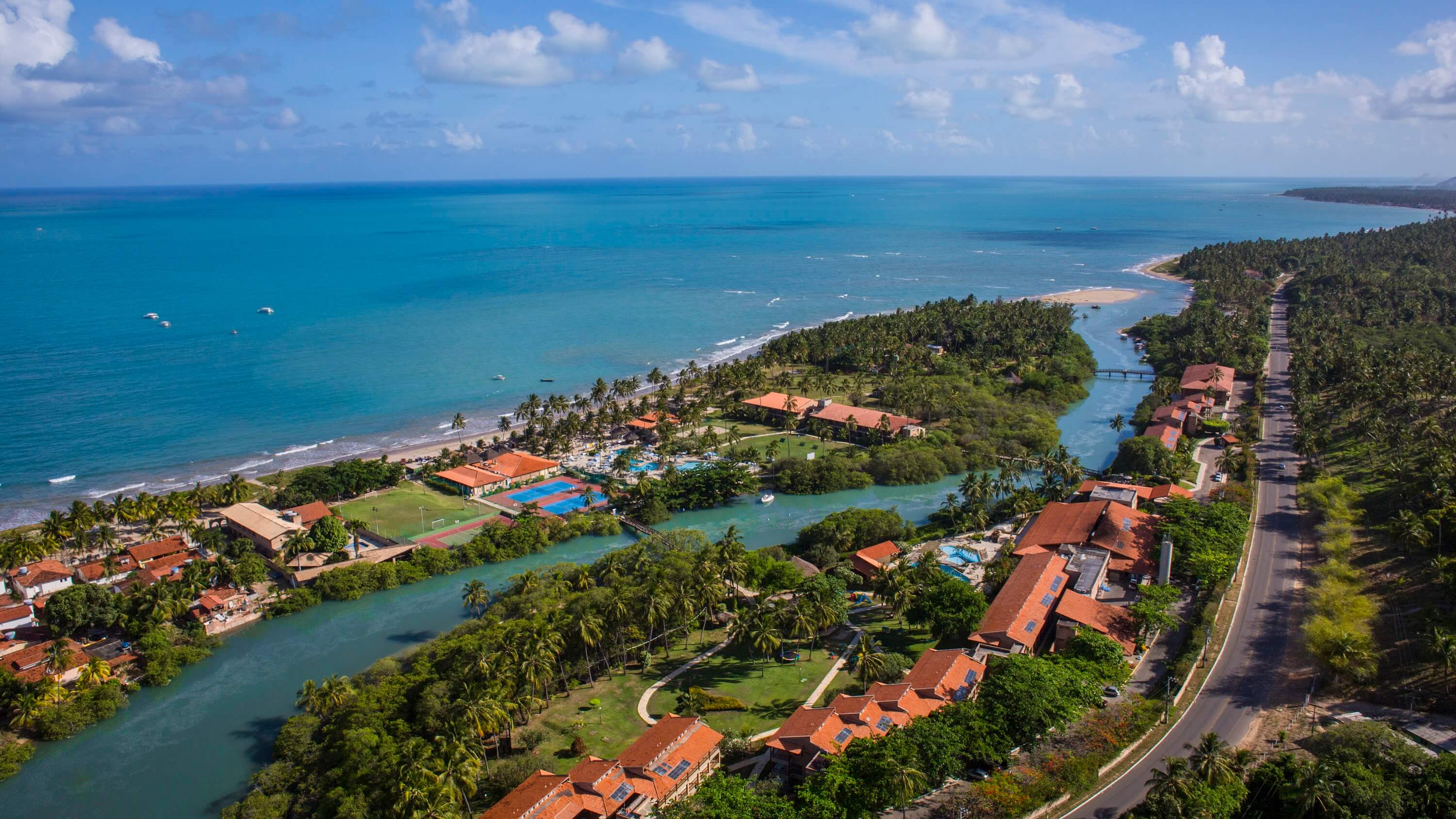 Vista aérea do resort de praia Salinas Maragogi, com acomodações tecnológicas, complexo de piscinas e ampla vegetação ao redor.